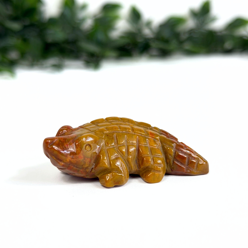 Mookaite crocodile carving on a white surface with green foliage in the background
