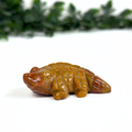 Mookaite crocodile carving on a white surface with green foliage in the background