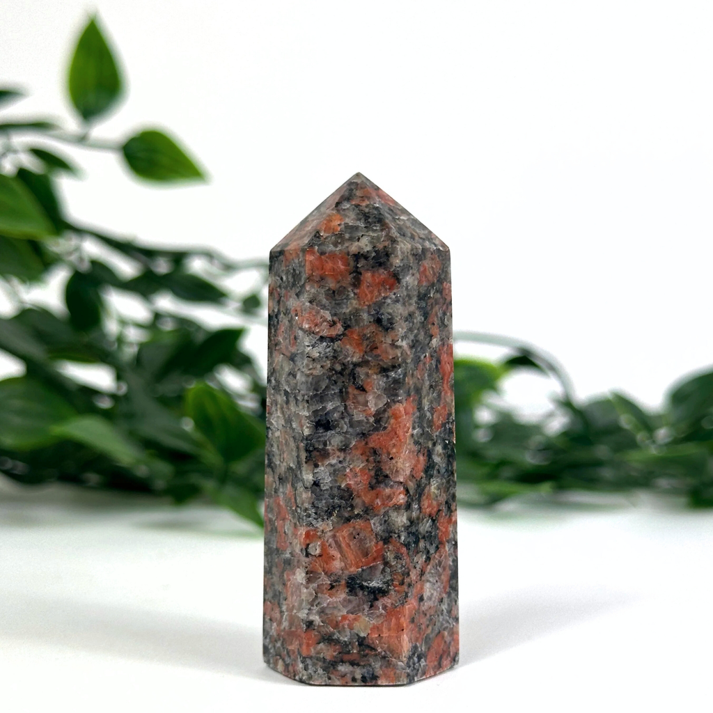 Feldspar crystal tower with red and black patterns on a white background with green leaves.