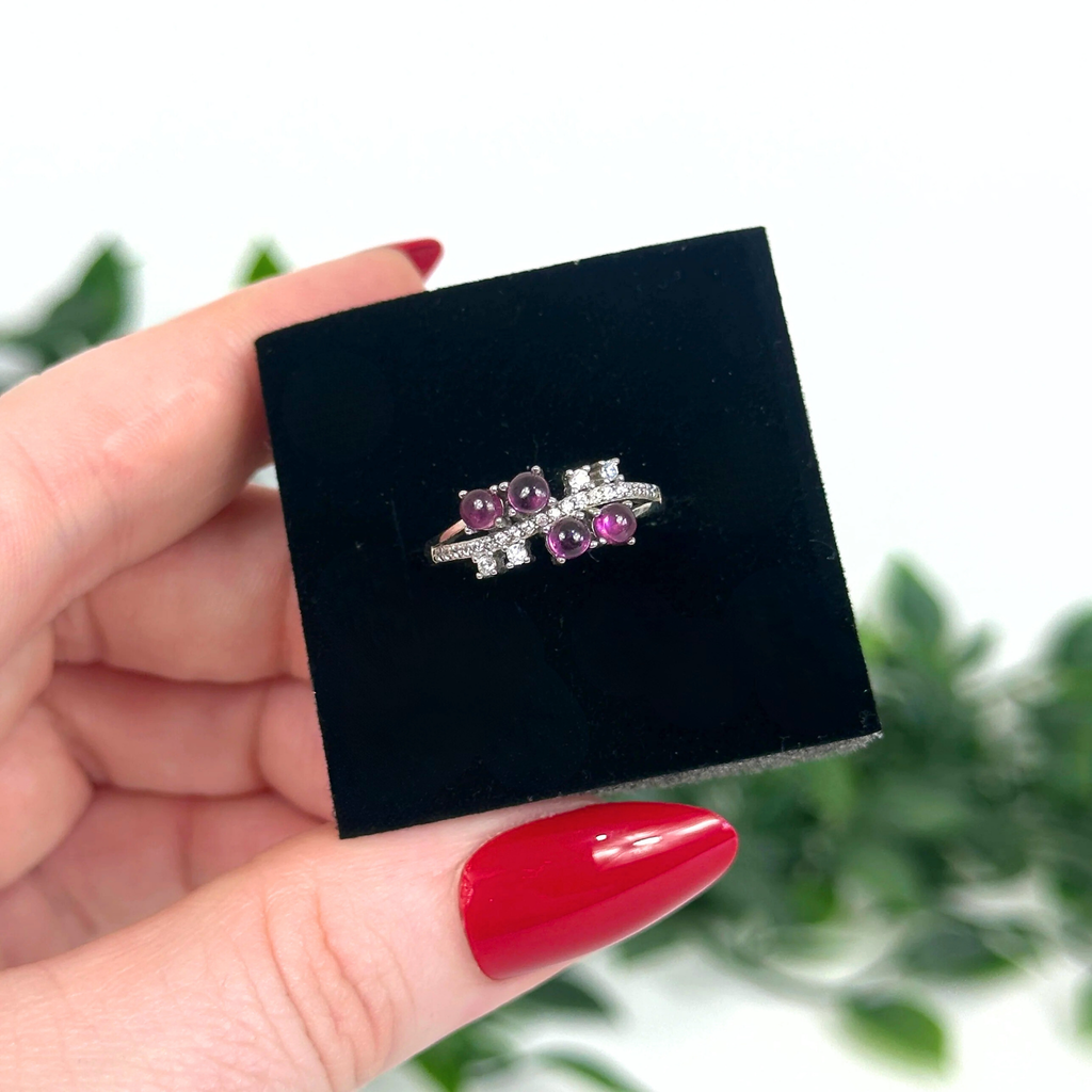 Silver ring with purple garnets on a black velvet box held by a hand with red nail polish.