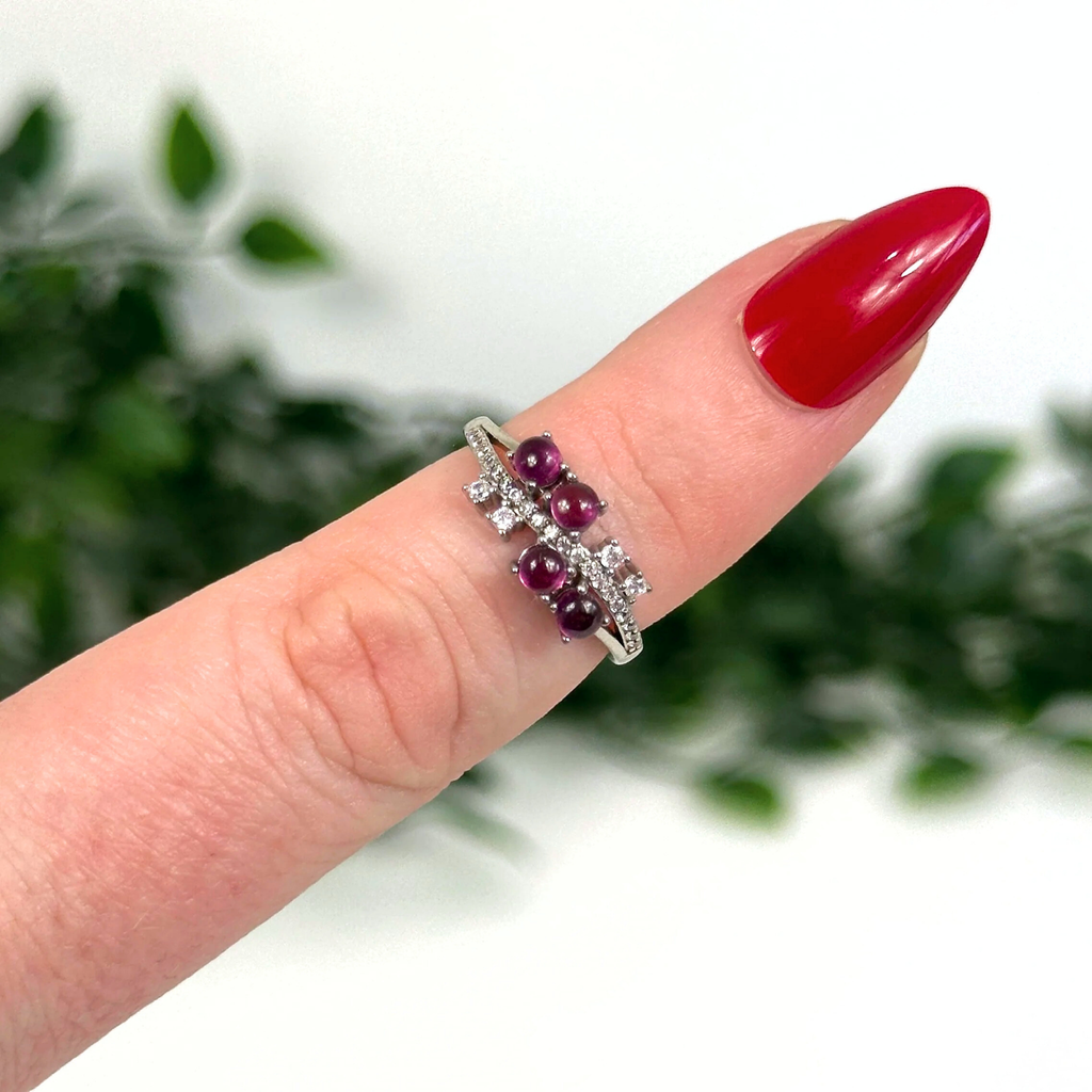 Silver ring with purple garnets on a finger against a blurred green background