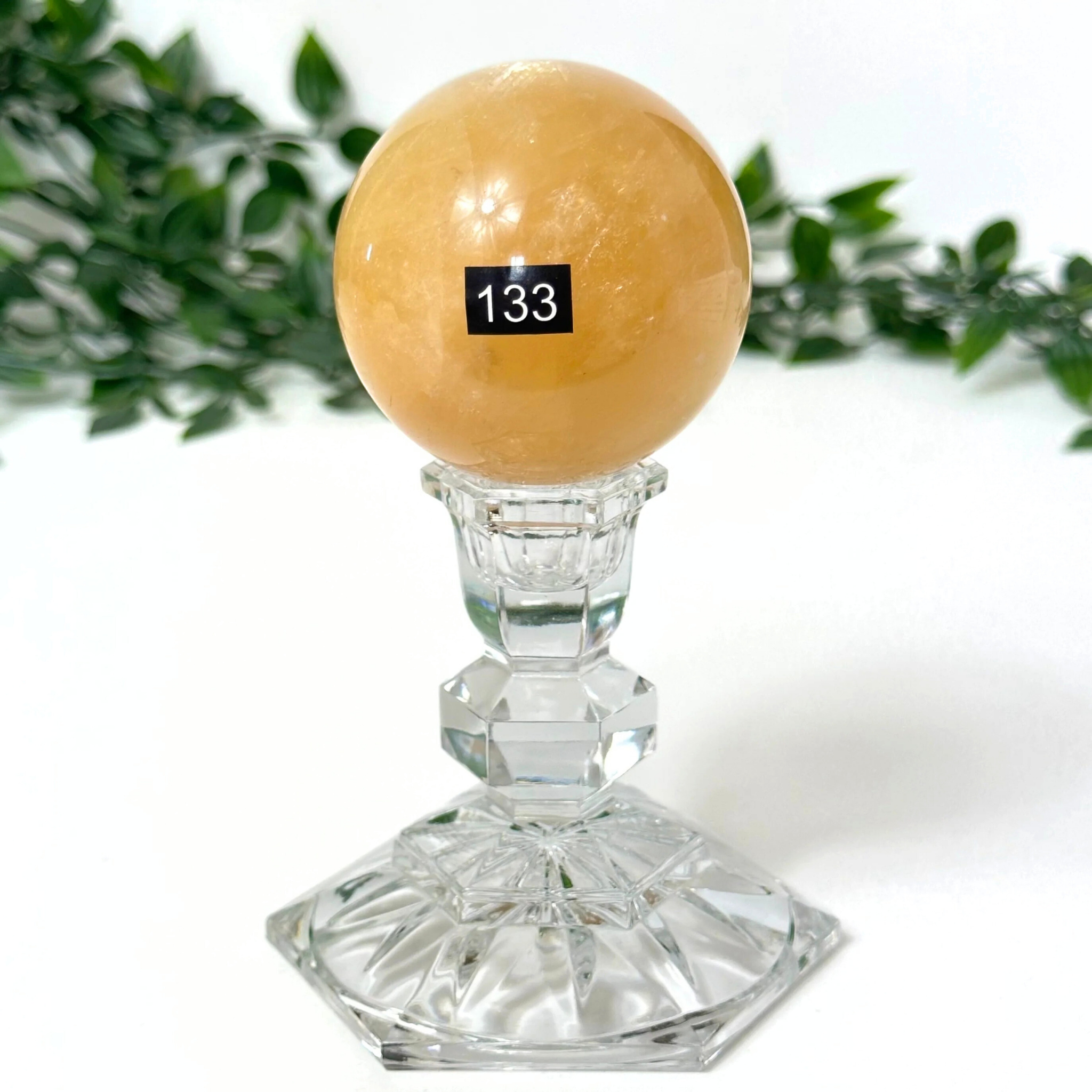 Crystal stand with a honey calcite crystal sphere against a white background