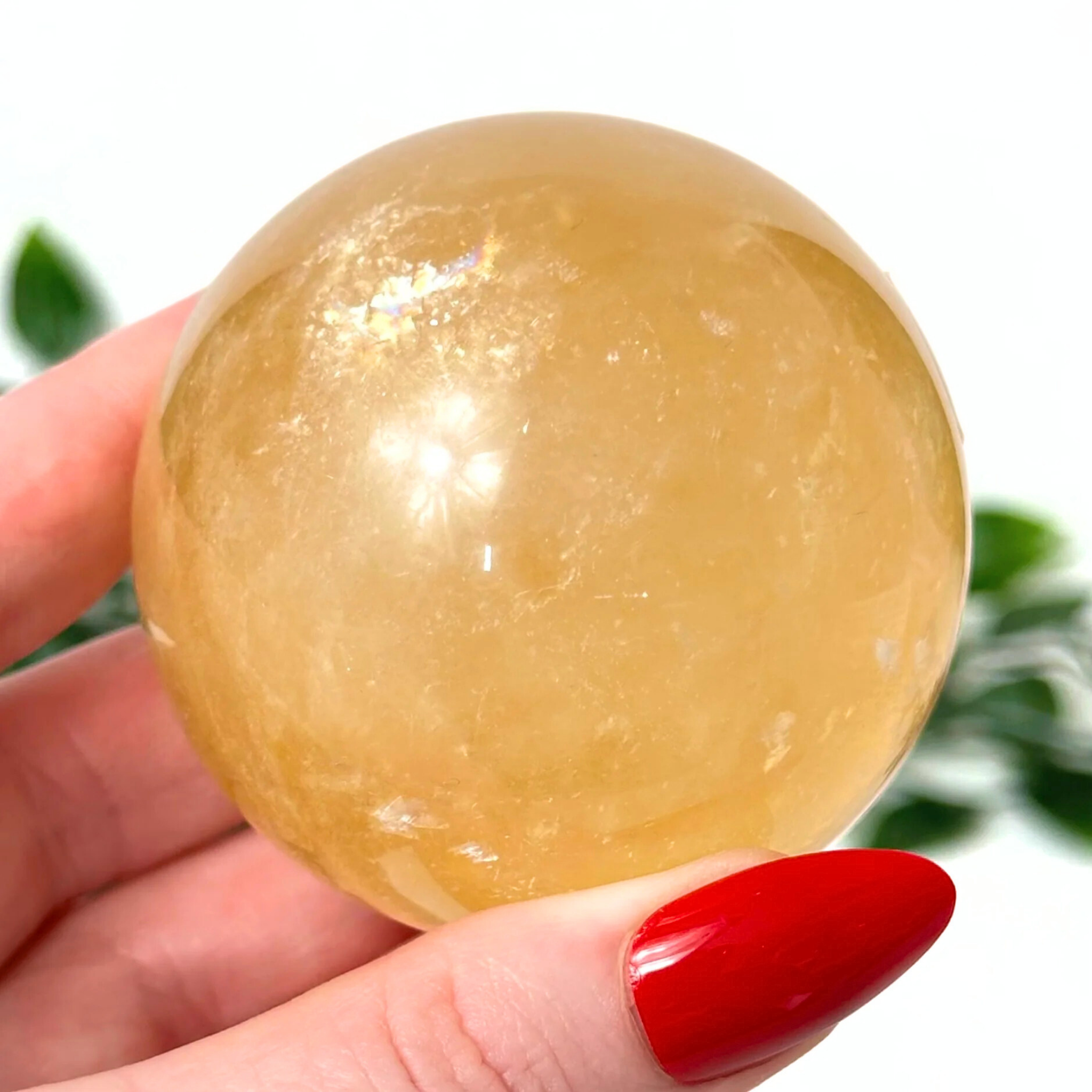 Hand holding a honey calcite crystal ball with a blurred green background