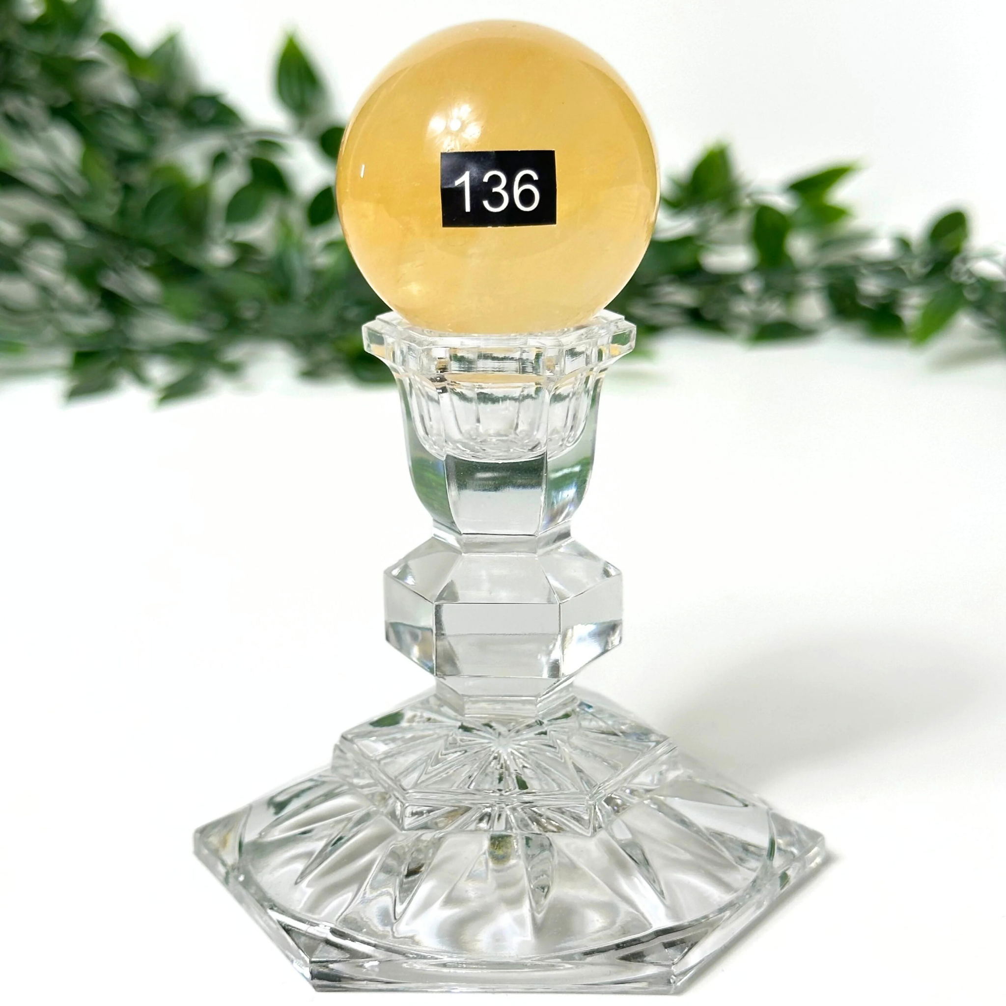 A honey calcite crystal sphere and crystal base on a white background