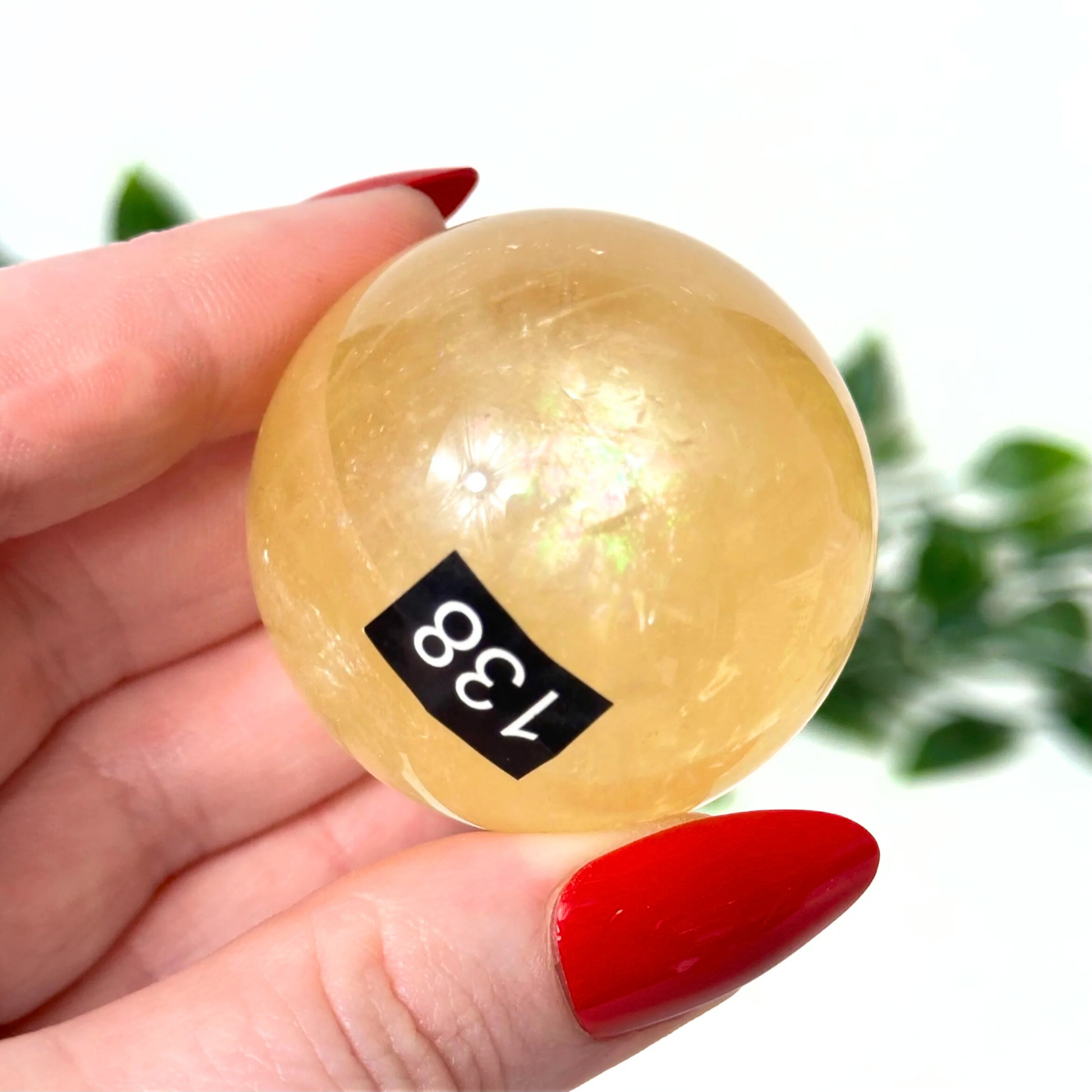 Hand holding a honey calcite crystal ball against a blurred green background
