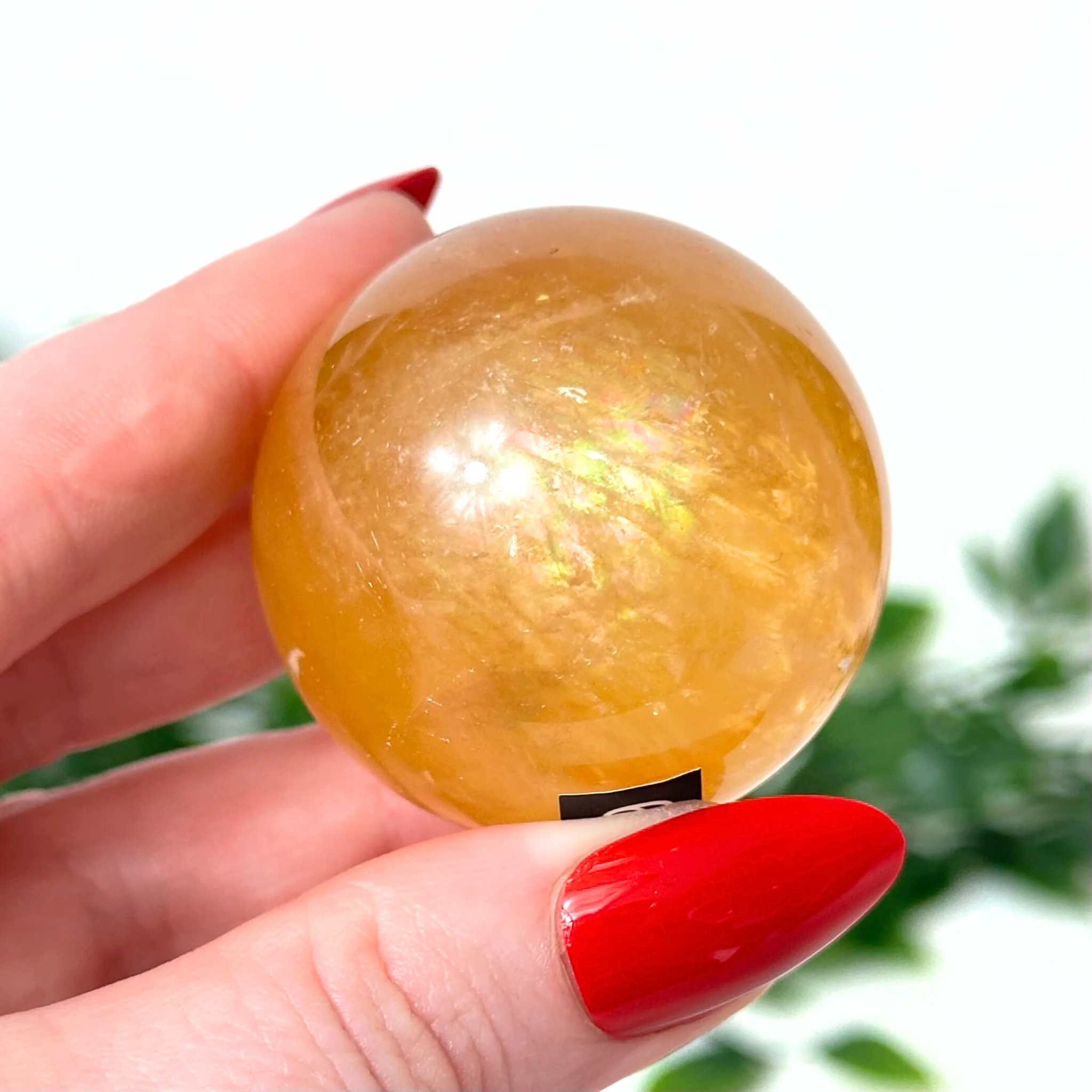 Hand holding a yellow honey calcite ball with a blurred green background