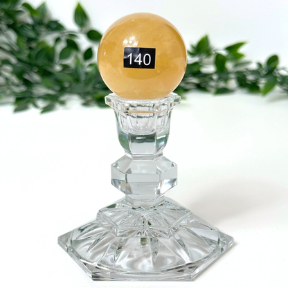 Honey calcite sphere on crystal stand on a white background