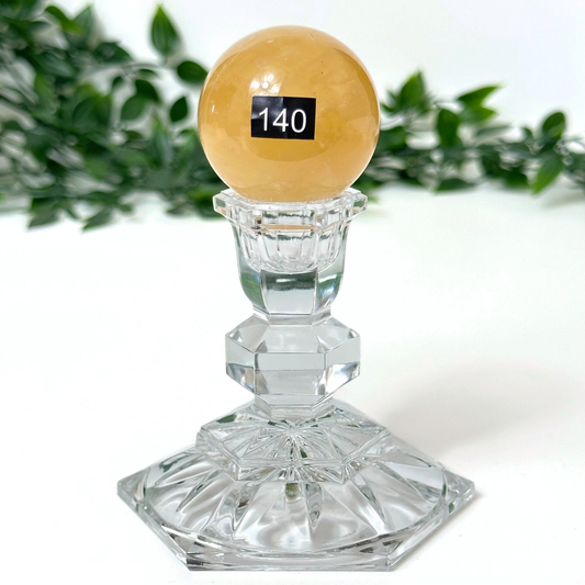 Honey calcite sphere on crystal stand on a white background