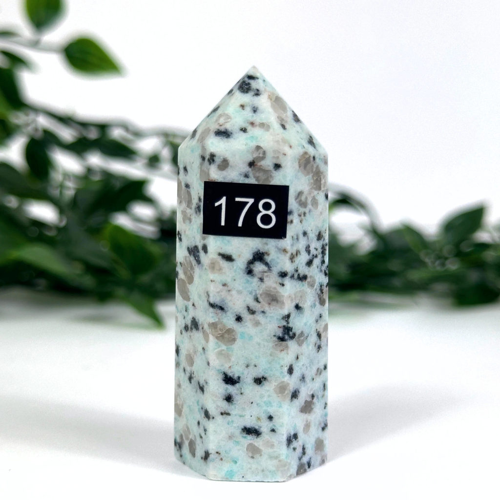 Kiwi jasper stone tower against a white background with greenery.