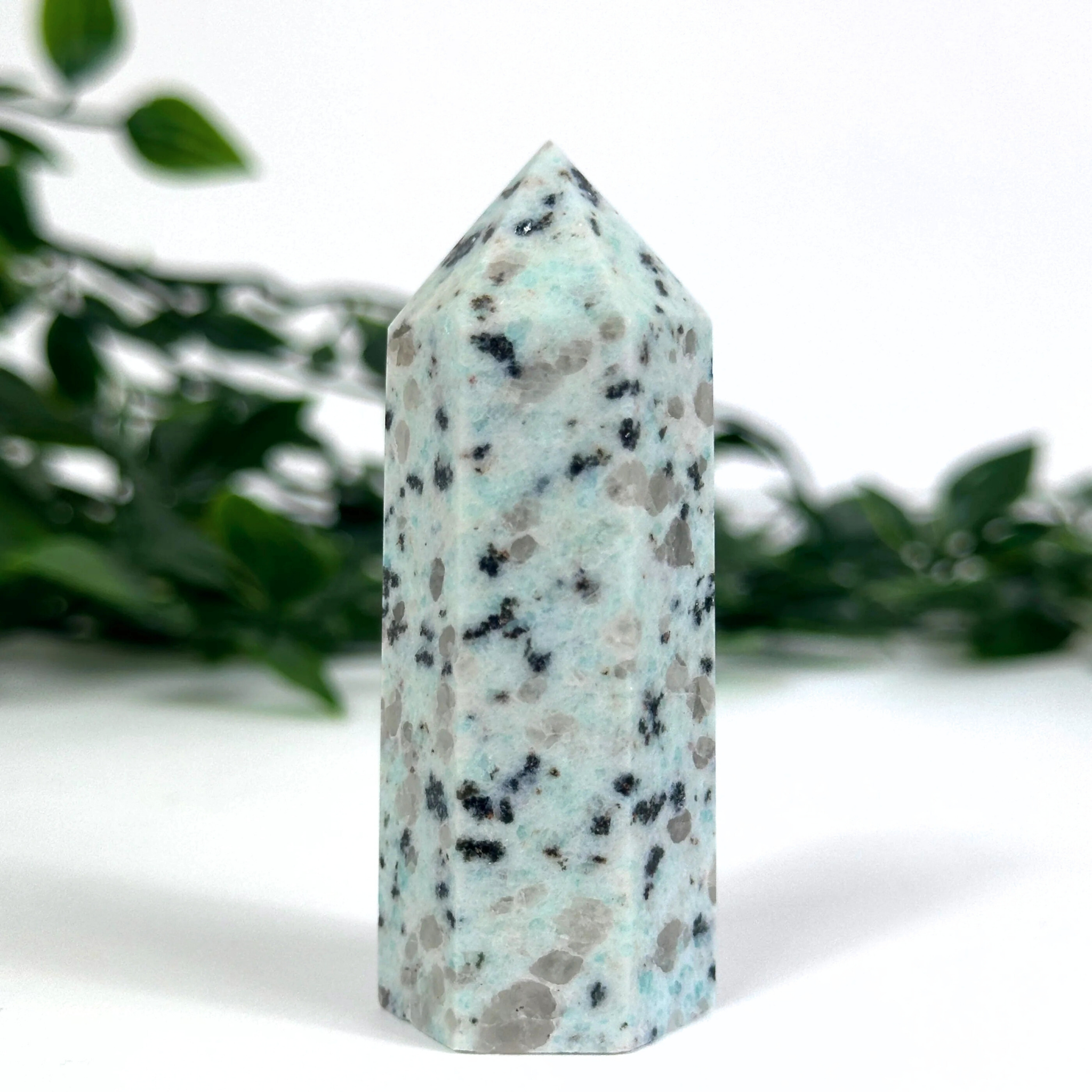 Kiwi jasper crystal tower on a white surface with blurred greenery in the background