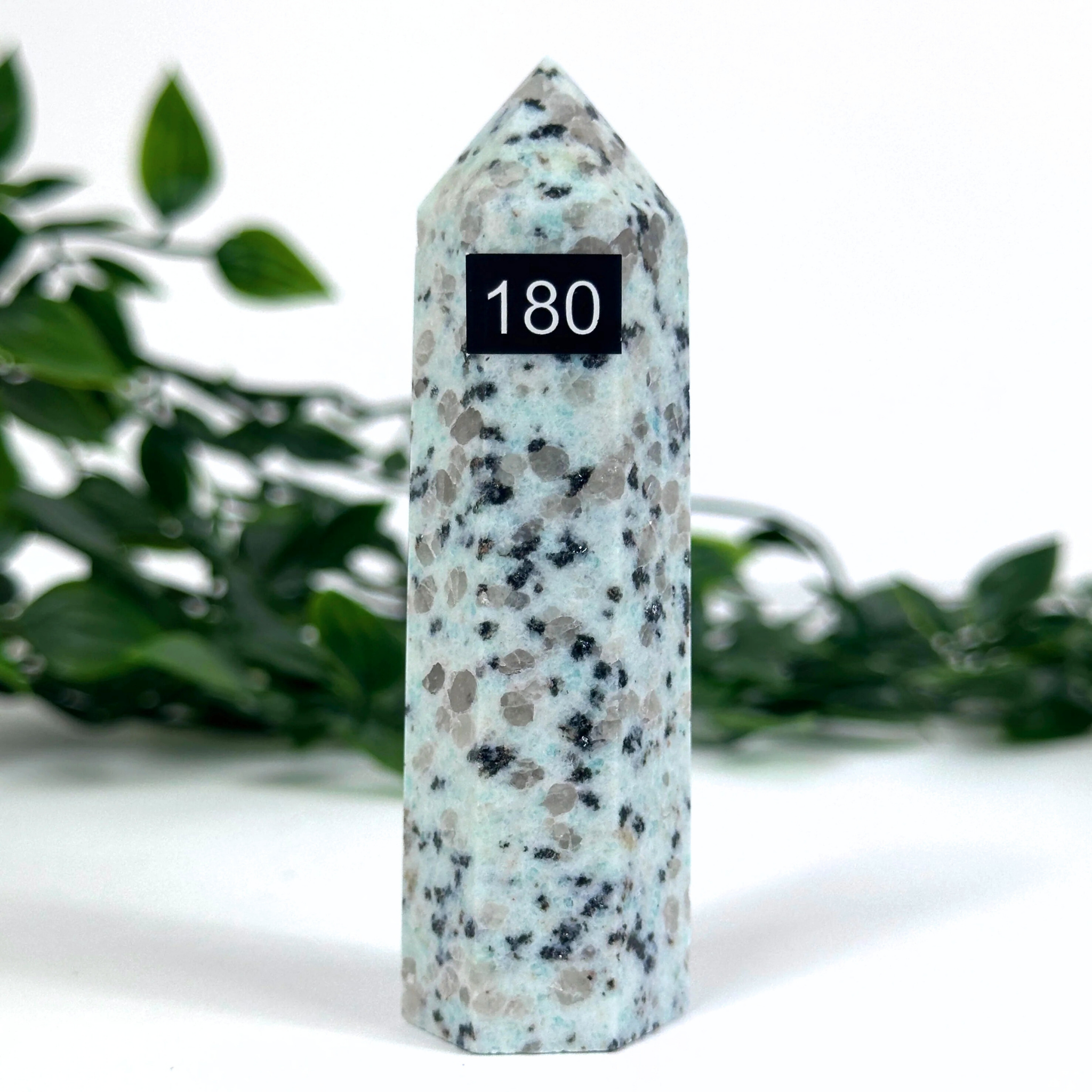 Kiwi jasper crystal tower with a black label displaying '180' on a white background with greenery.