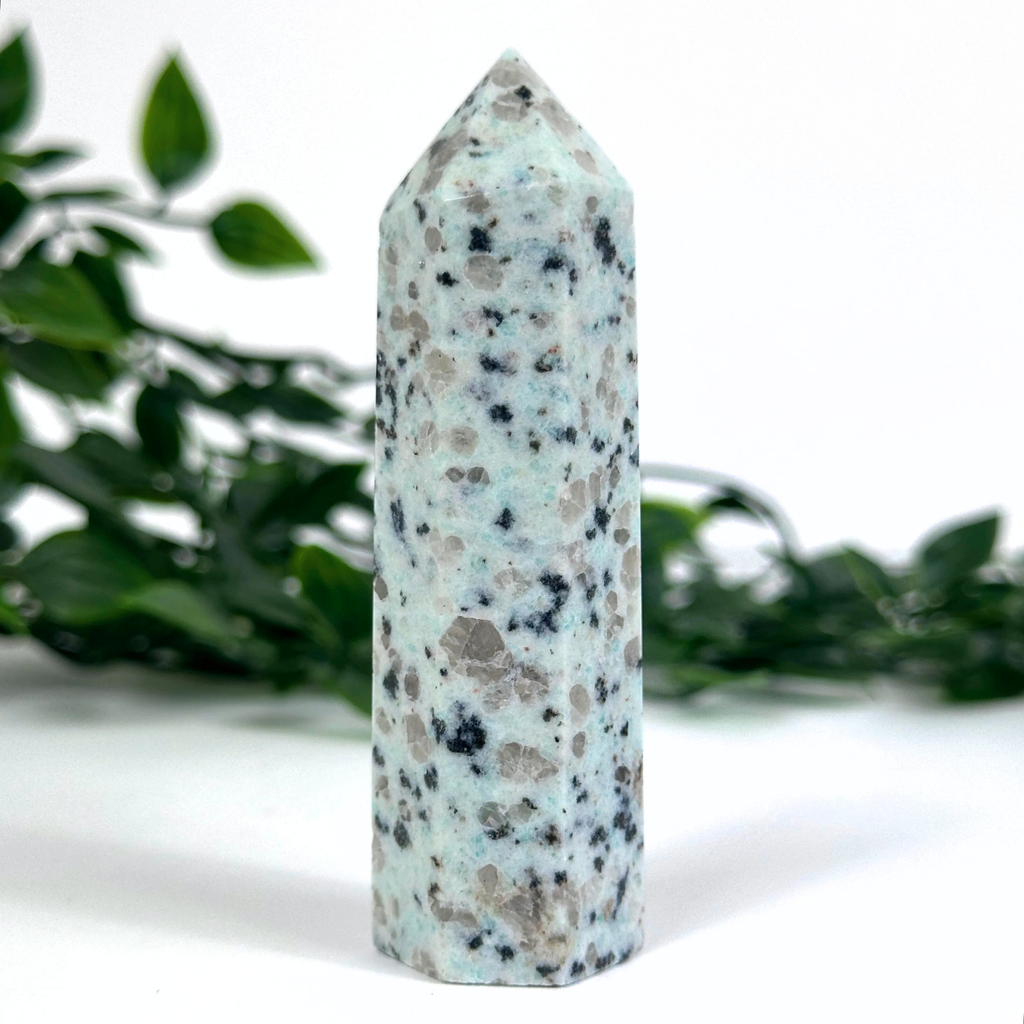 Kiwi jasper crystal tower on a white surface with green foliage in the background