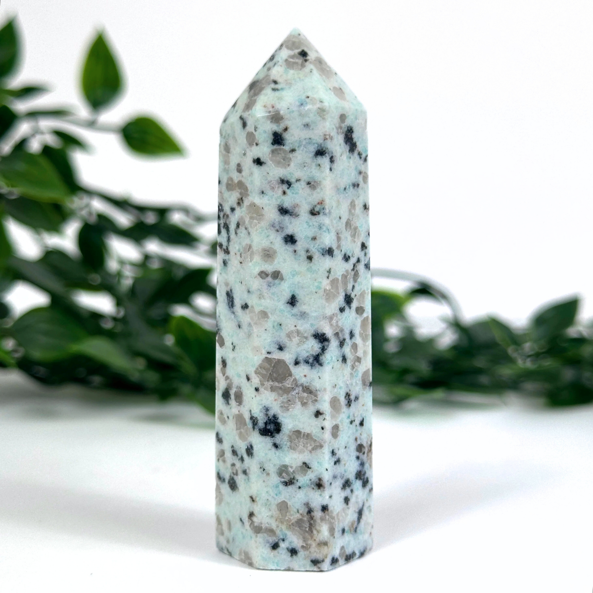 Kiwi jasper crystal tower on a white surface with green foliage in the background