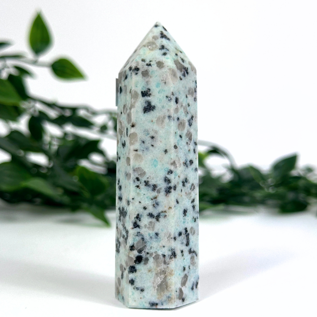 Kiwi jasper crystal tower on a white surface with greenery in the background