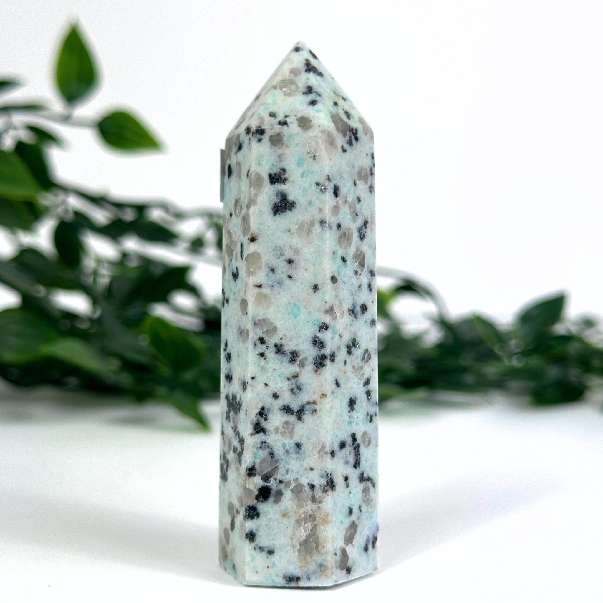 Kiwi jasper crystal tower on a white surface with greenery in the background