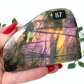 Multicolored labradorite stone held by a hand with red nail polish, against a white background.