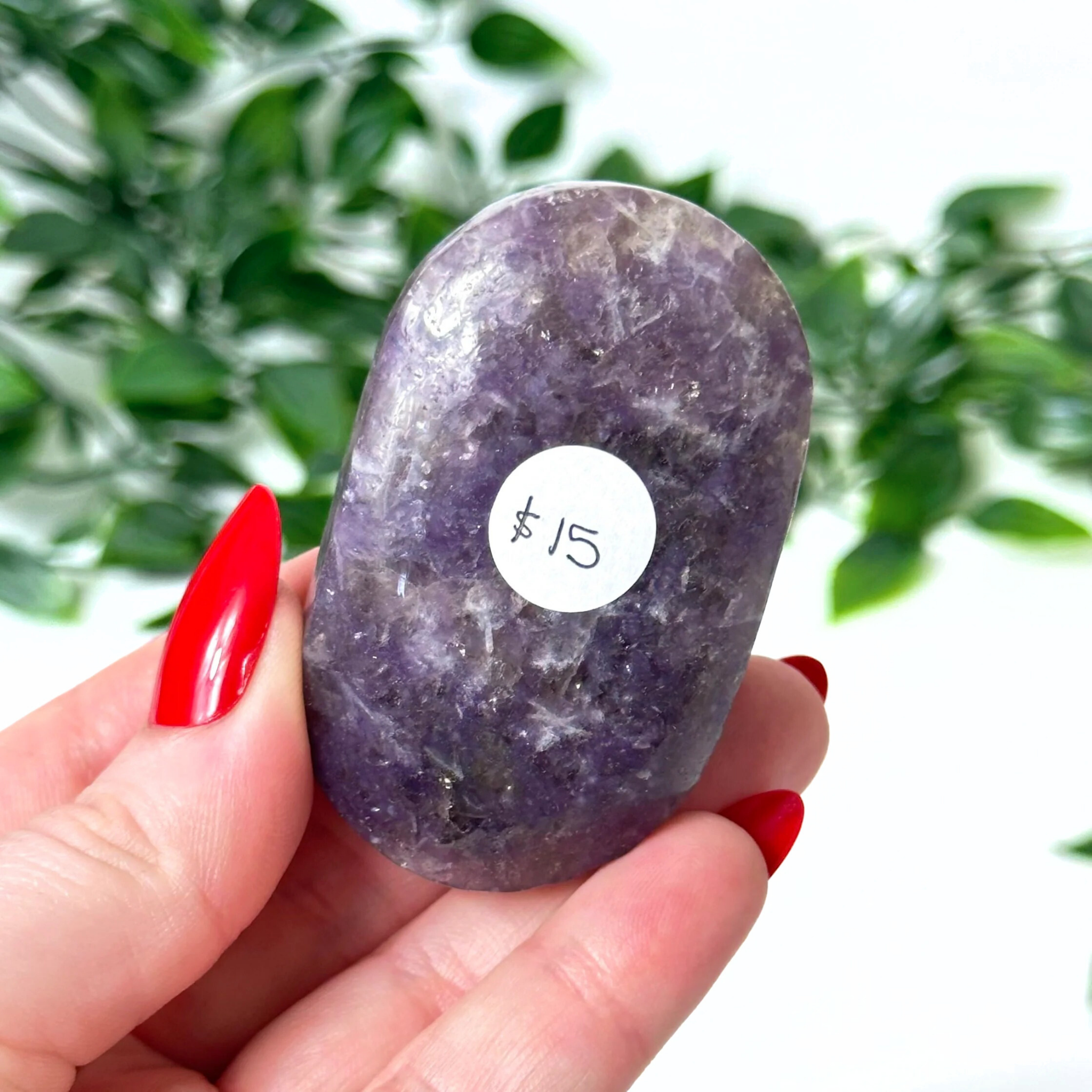 Lepidolite crystal held in a hand with a blurred green leafy background