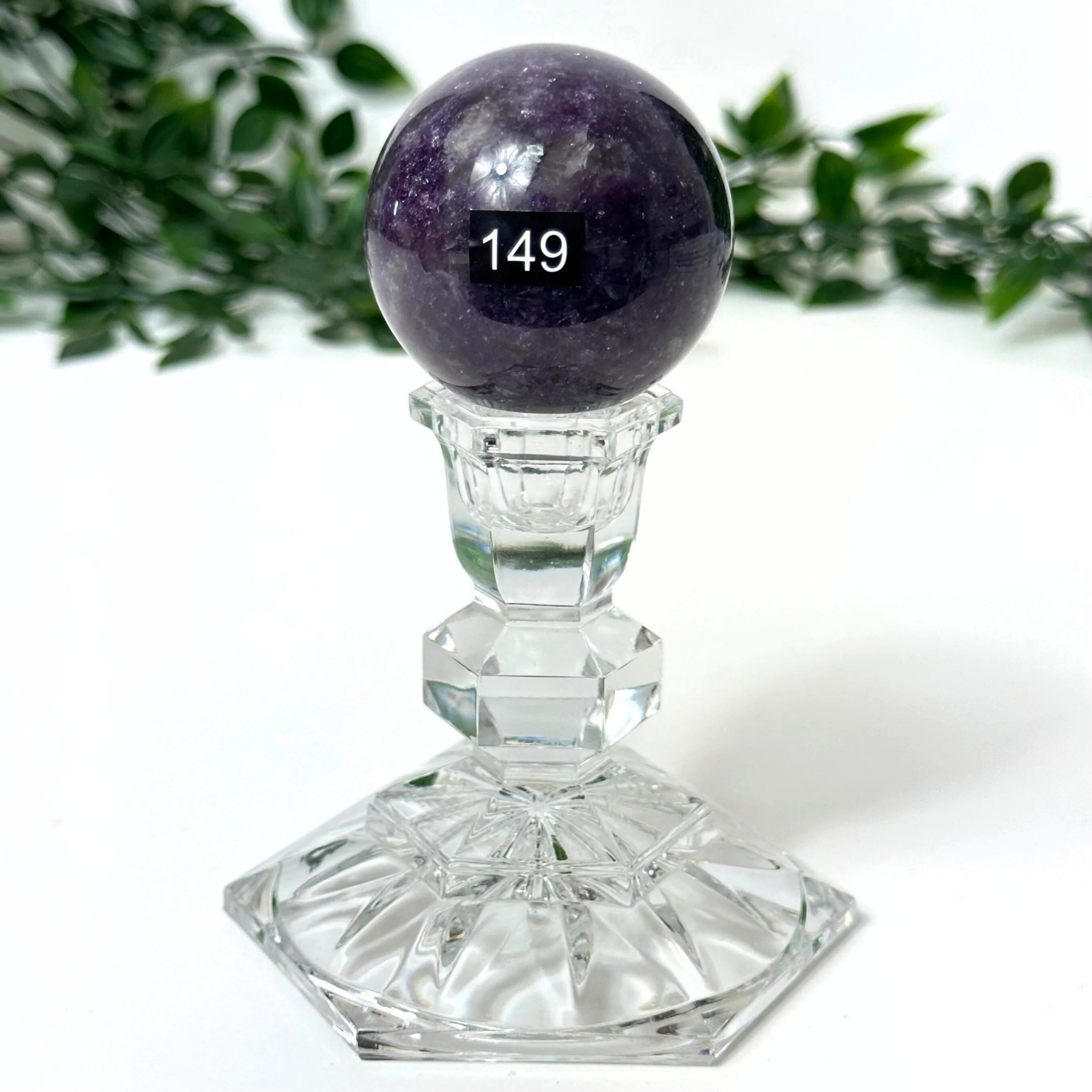 Crystal pedestal with a purple lepidolite sphere against a white background