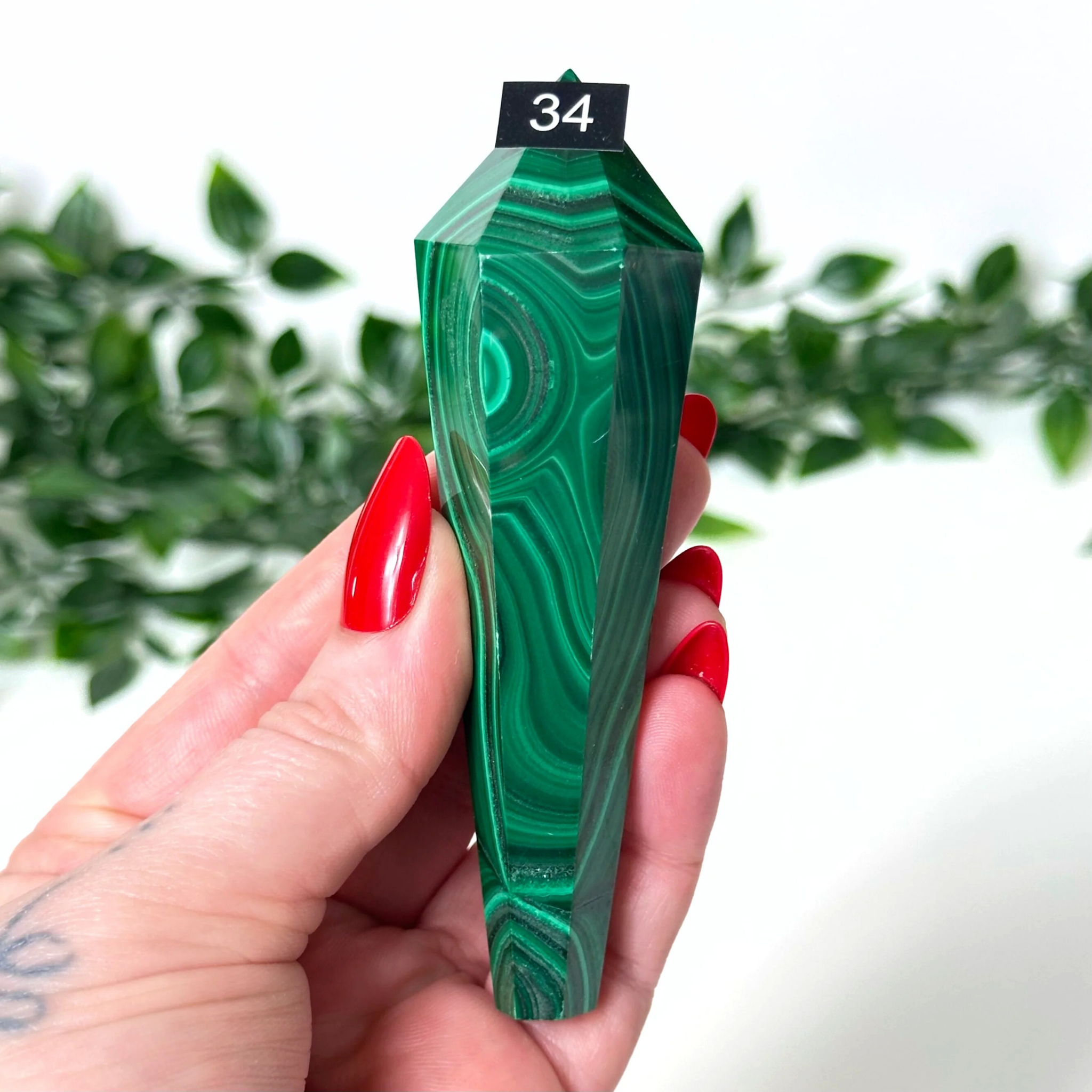 Hand holding a green malachite crystal wand with a blurred green plant background
