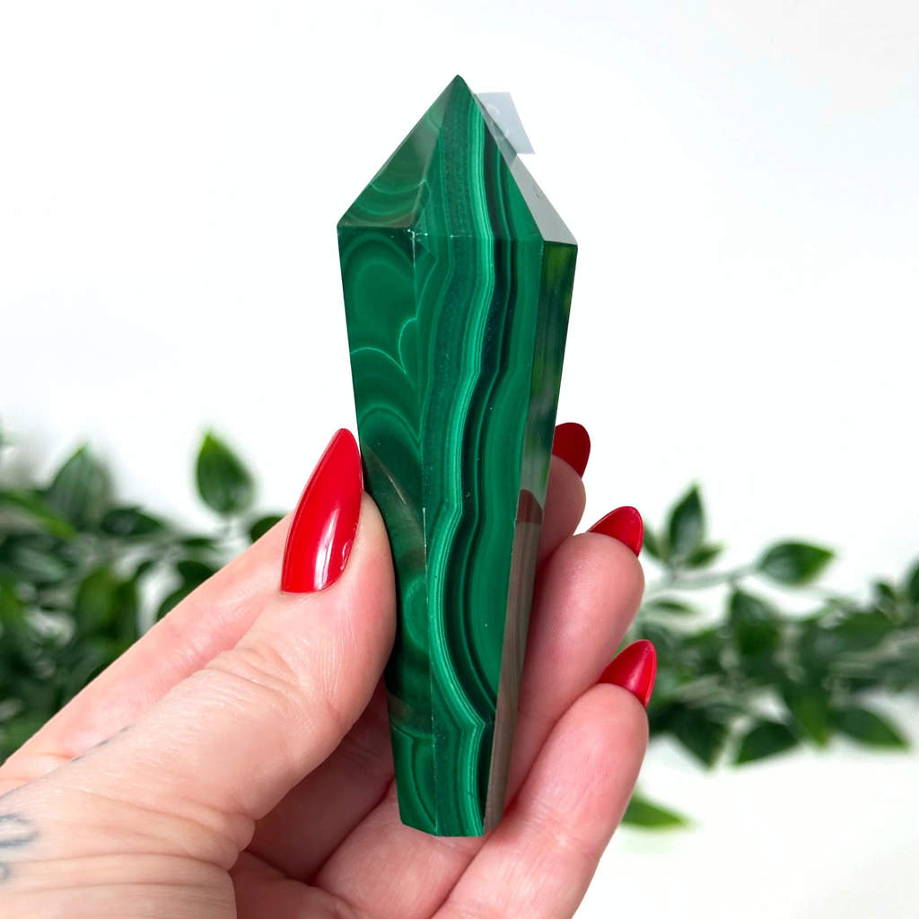 Hand holding a green malachite crystal with a blurred green plant background