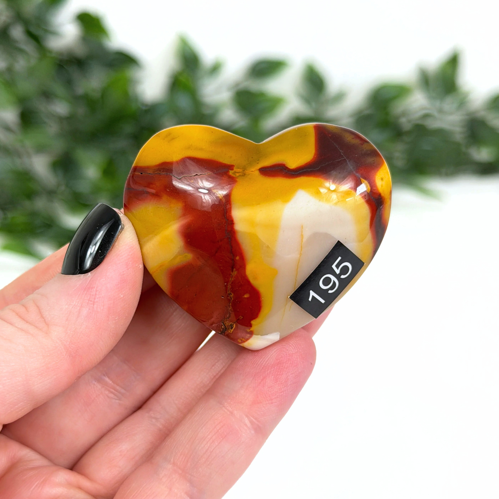 Heart-shaped mookaite stone held in a hand with a blurred green background