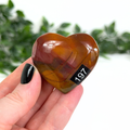 Heart-shaped mookaite stone held in a hand with a blurred green background