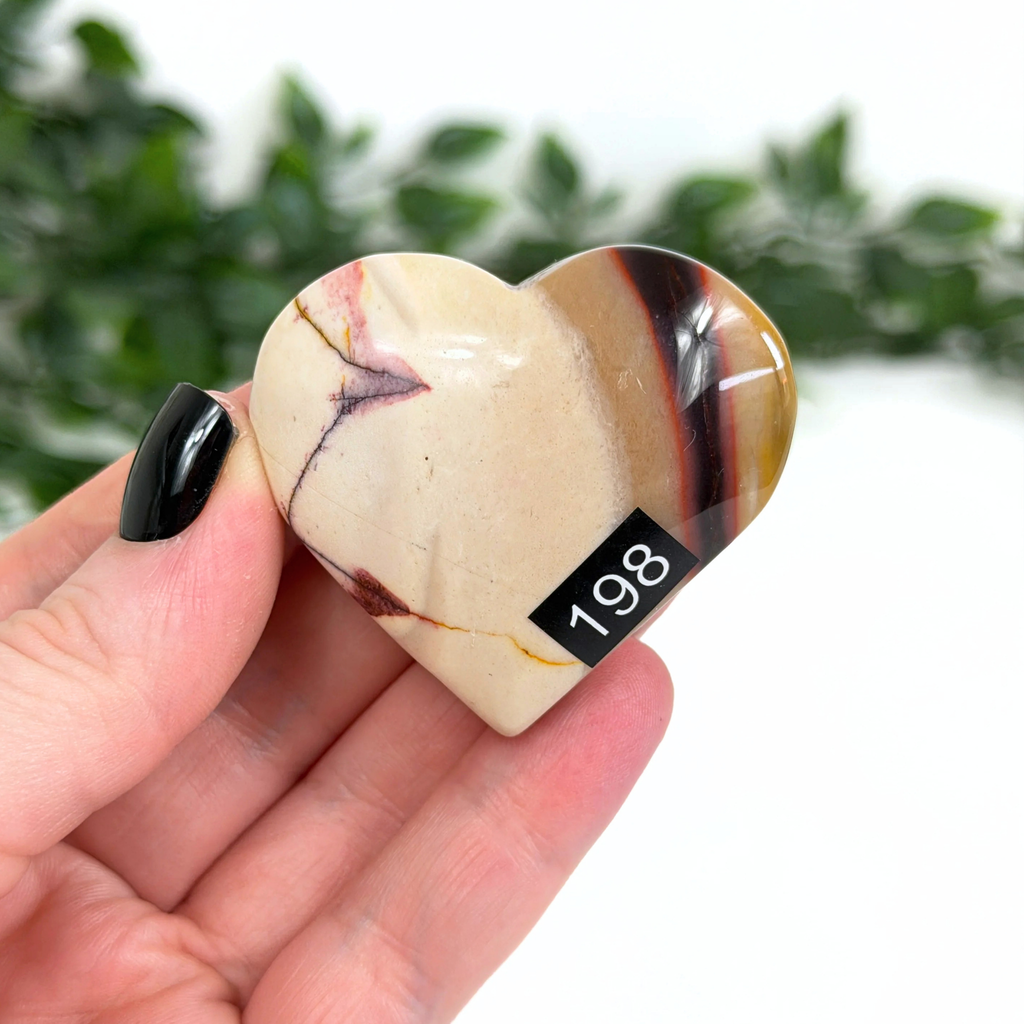 Heart-shaped mookaite stone held in a hand with a blurred green background