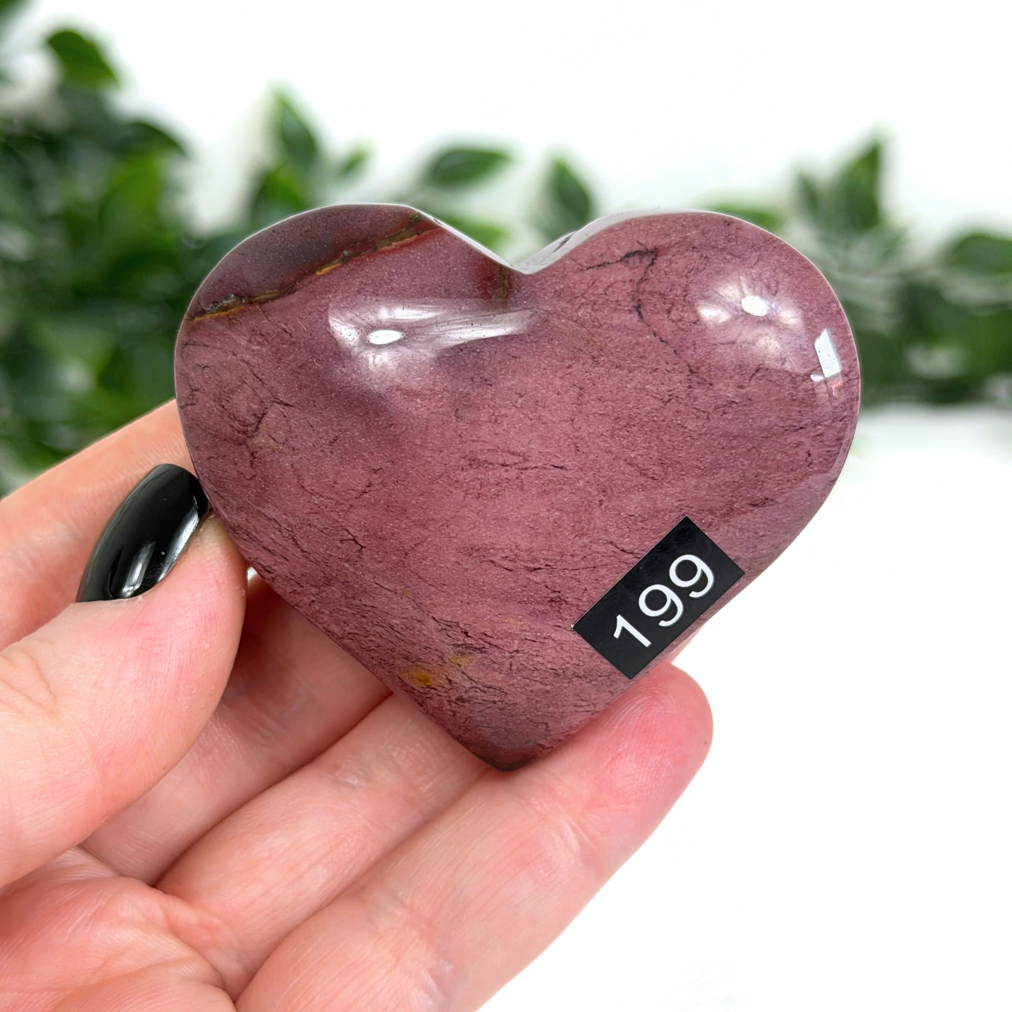 Heart-shaped purple mookaite stone held in a hand with a blurred green background