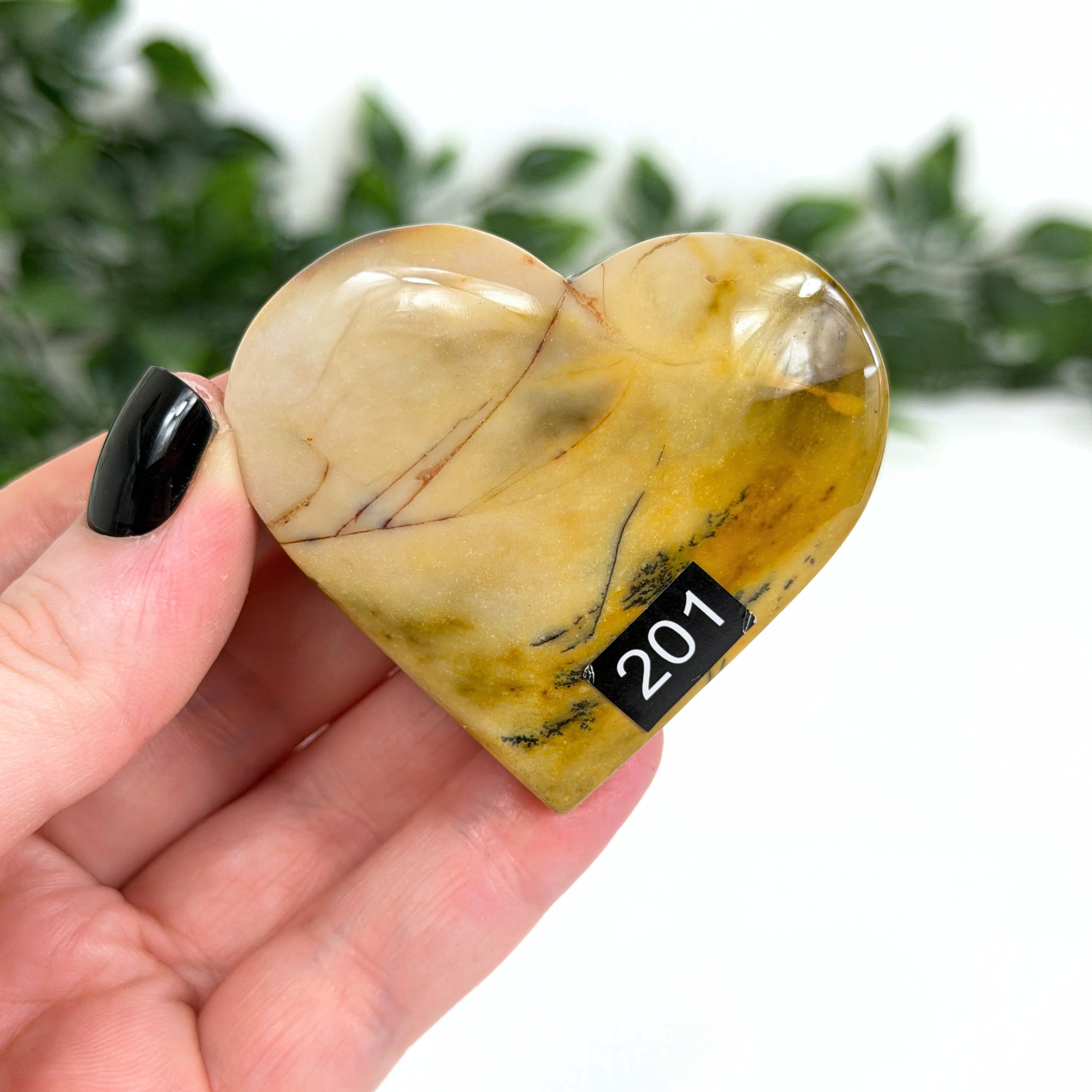 Heart-shaped mookaite crystal held in a hand with a blurred green background