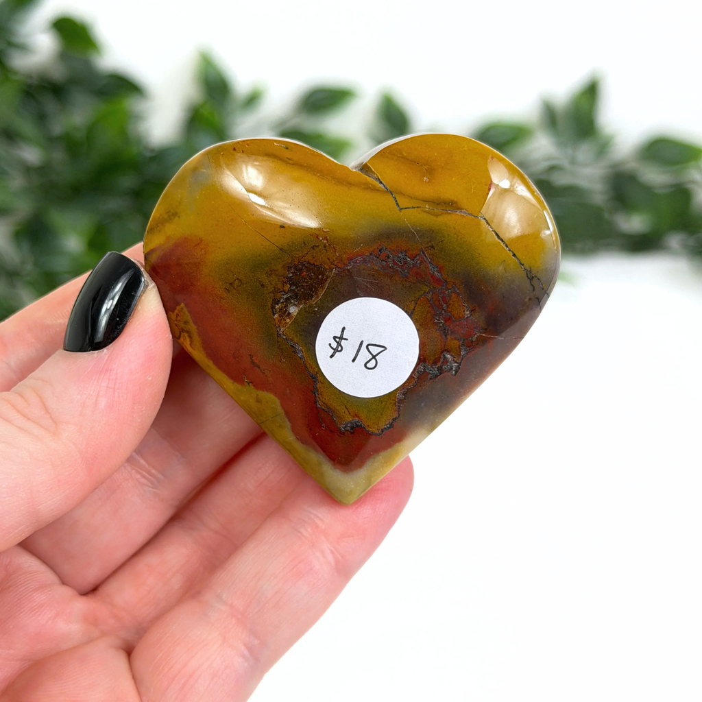 Heart-shaped mookaite crystal held in a hand with a price tag on a white background