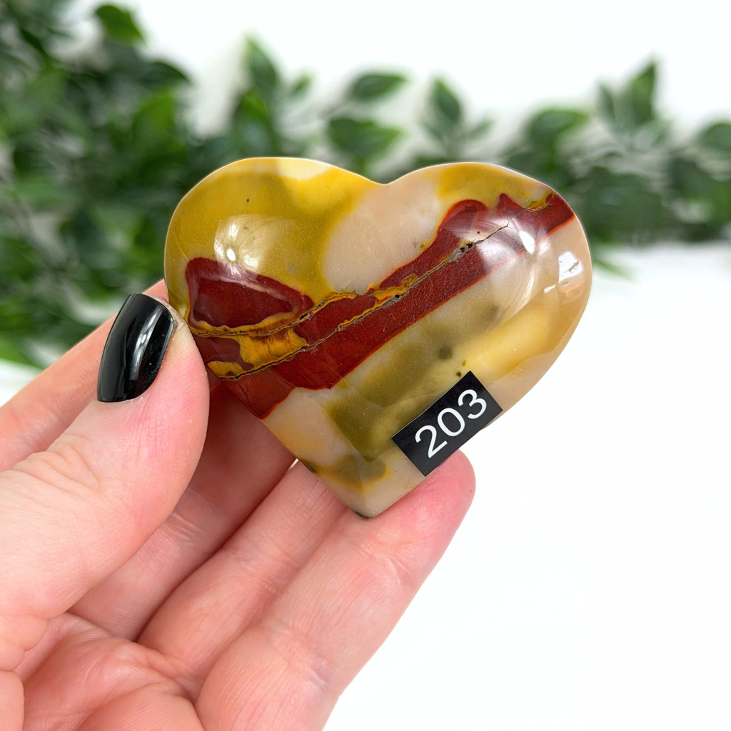 Heart-shaped marbled mookaite stone held in a hand with a blurred green background