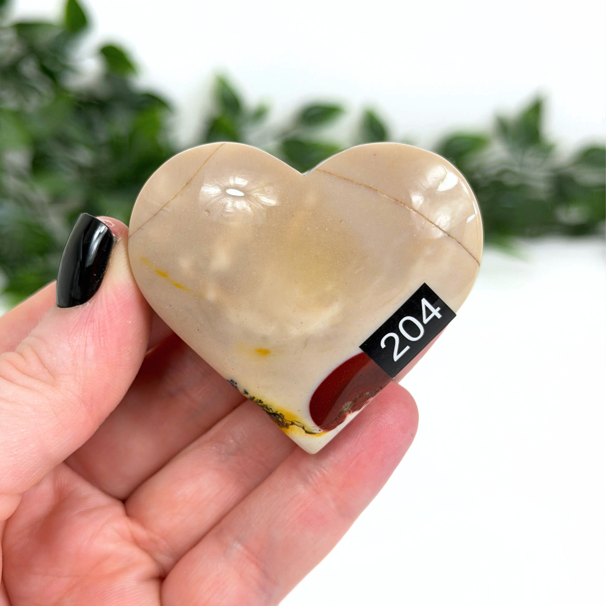Heart-shaped mookaite stone held in a hand with a blurred green background