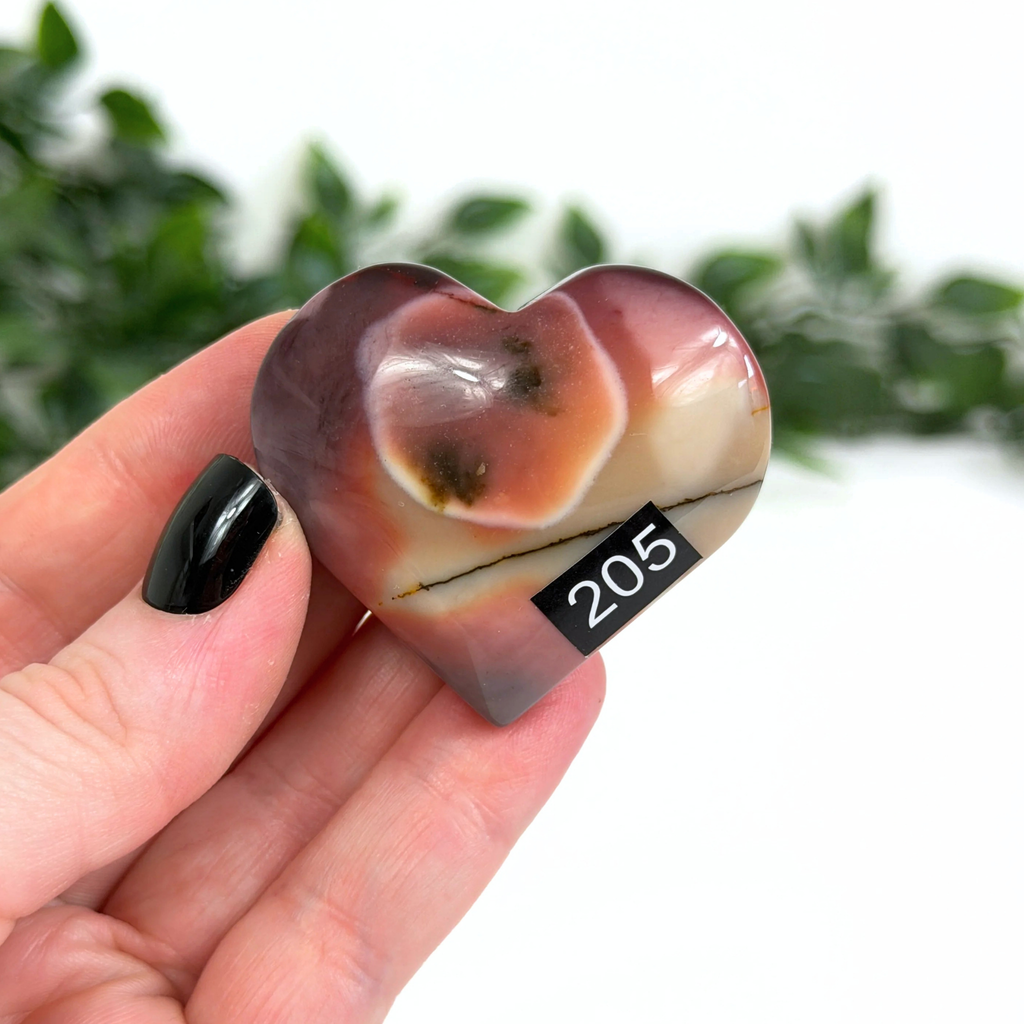 Hand holding a mookaite crystal heart with a white leafy background