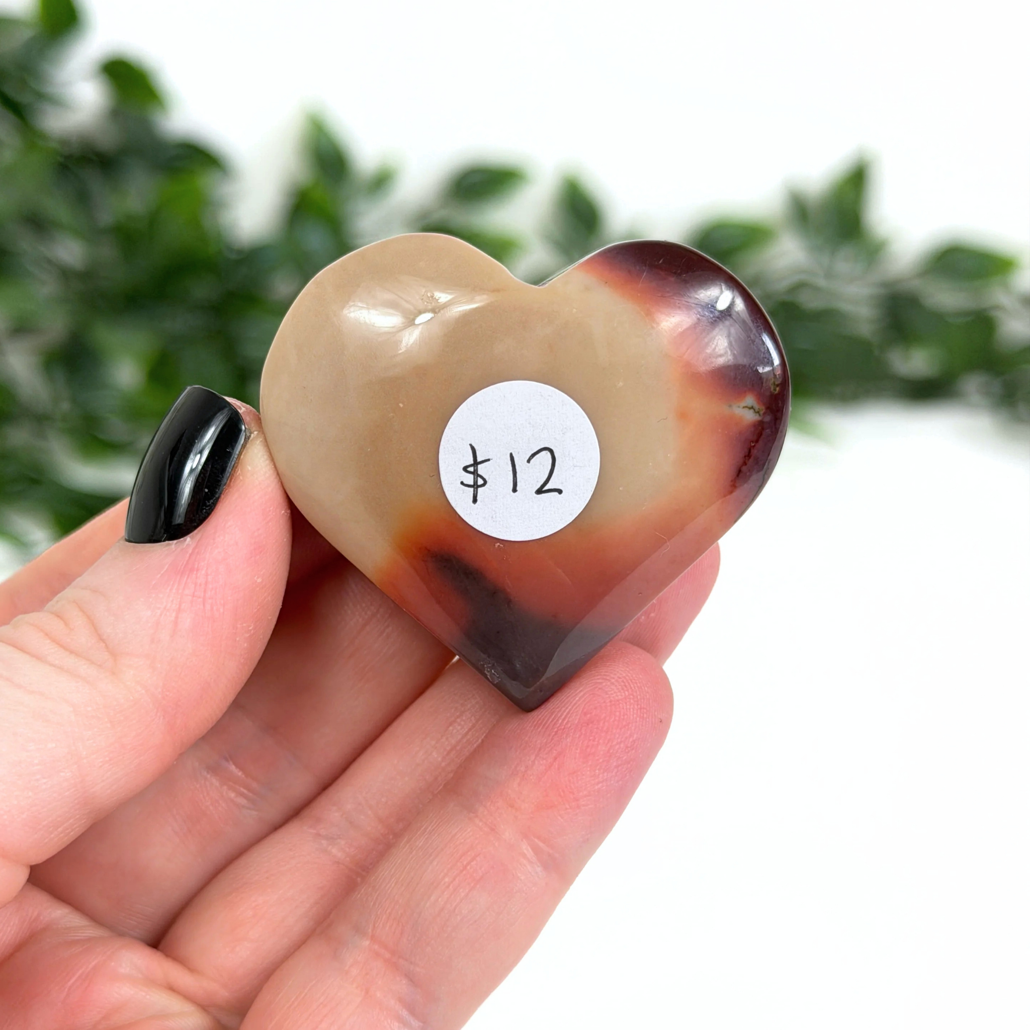Heart-shaped mookaite stone with a price tag held in a hand against a blurred green background