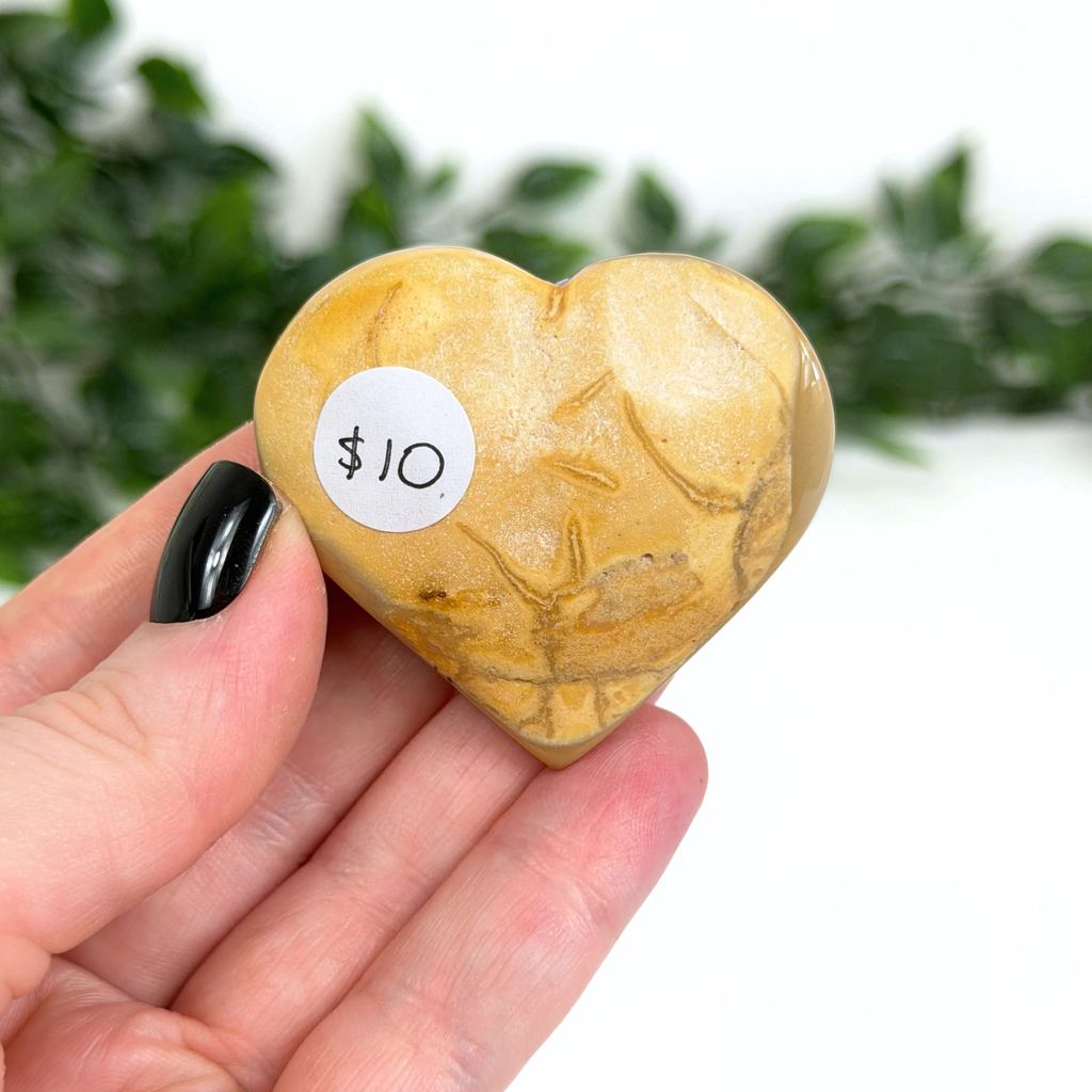 Heart-shaped mookaite stone with a $10 sticker held in a hand against a blurred green background