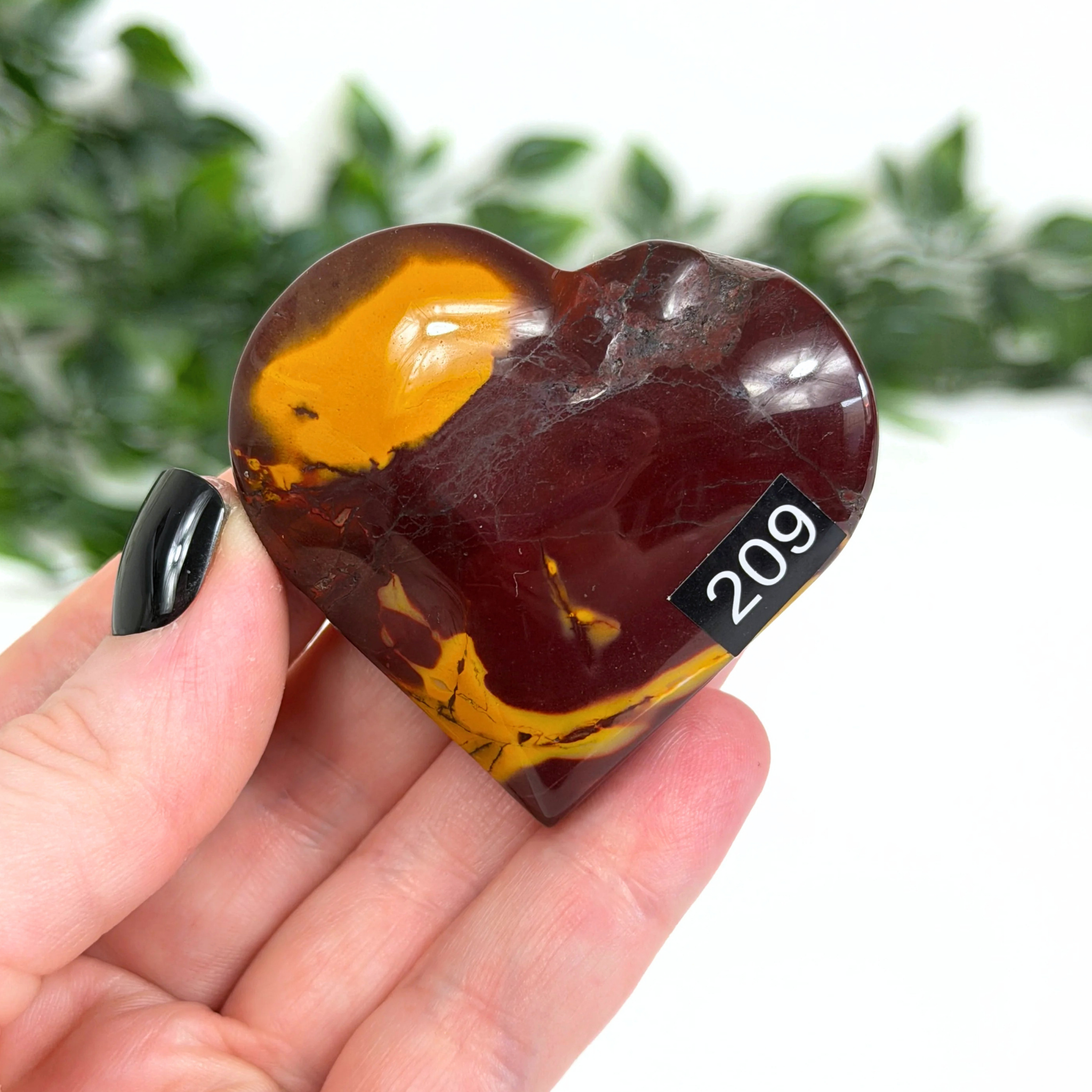 Heart-shaped mookaite stone held in a hand with a blurred green background