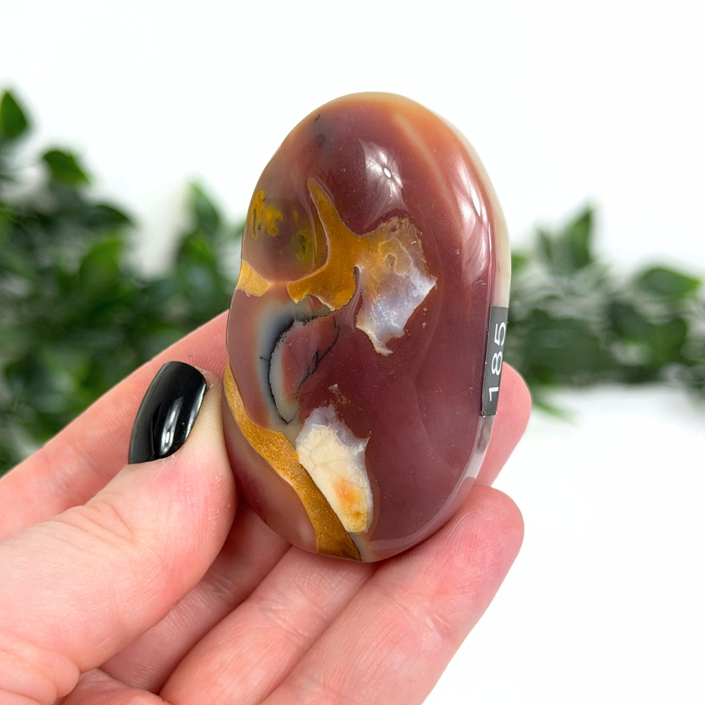 Hand holding a mookaite palm stone with a blurred green background