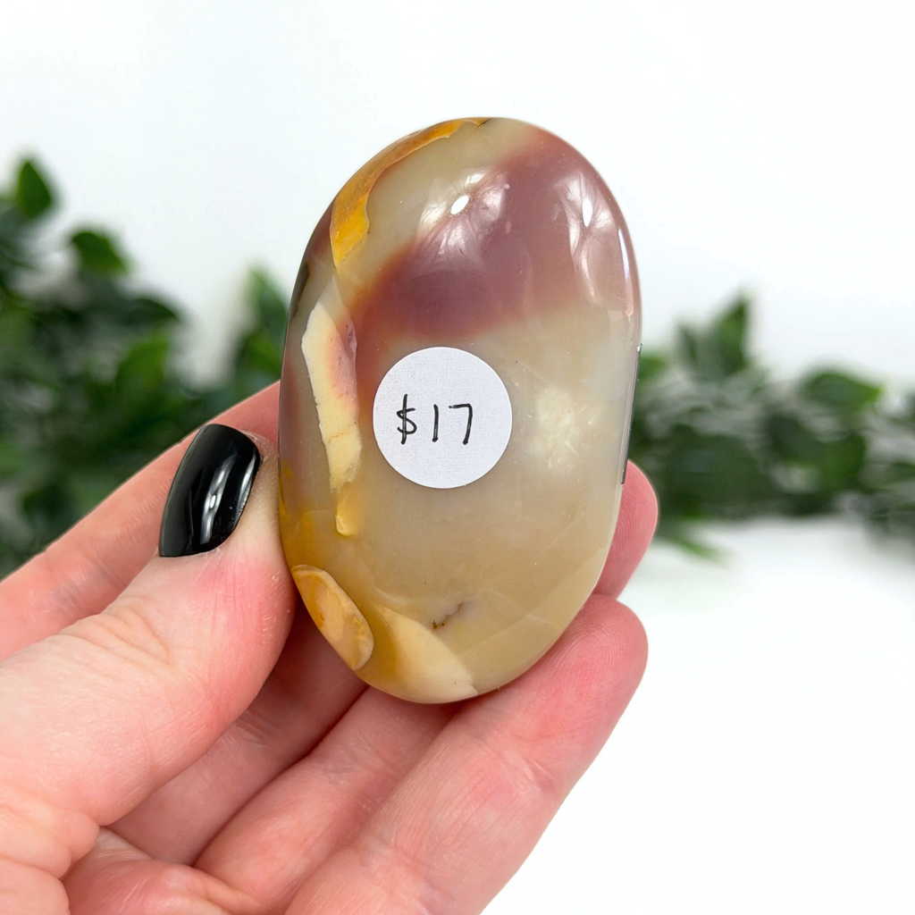 Hand holding a mookaite palm stone with a price tag sticker on a white background