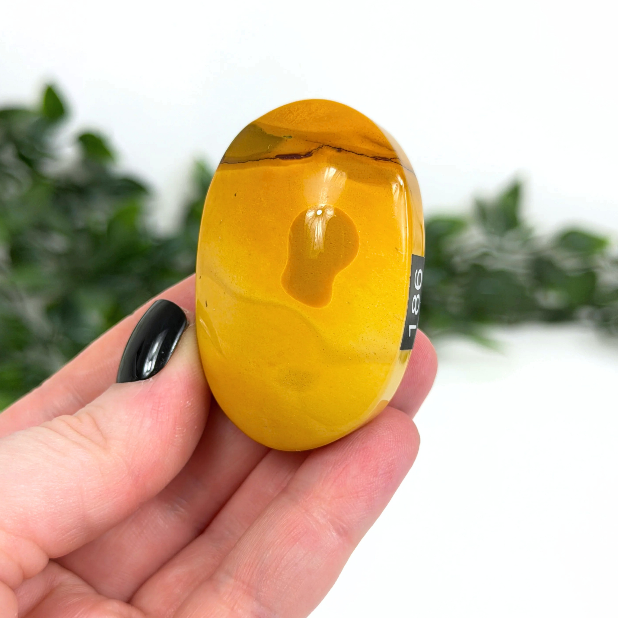 Hand holding a yellow mookaite palm stone with a blurred green background