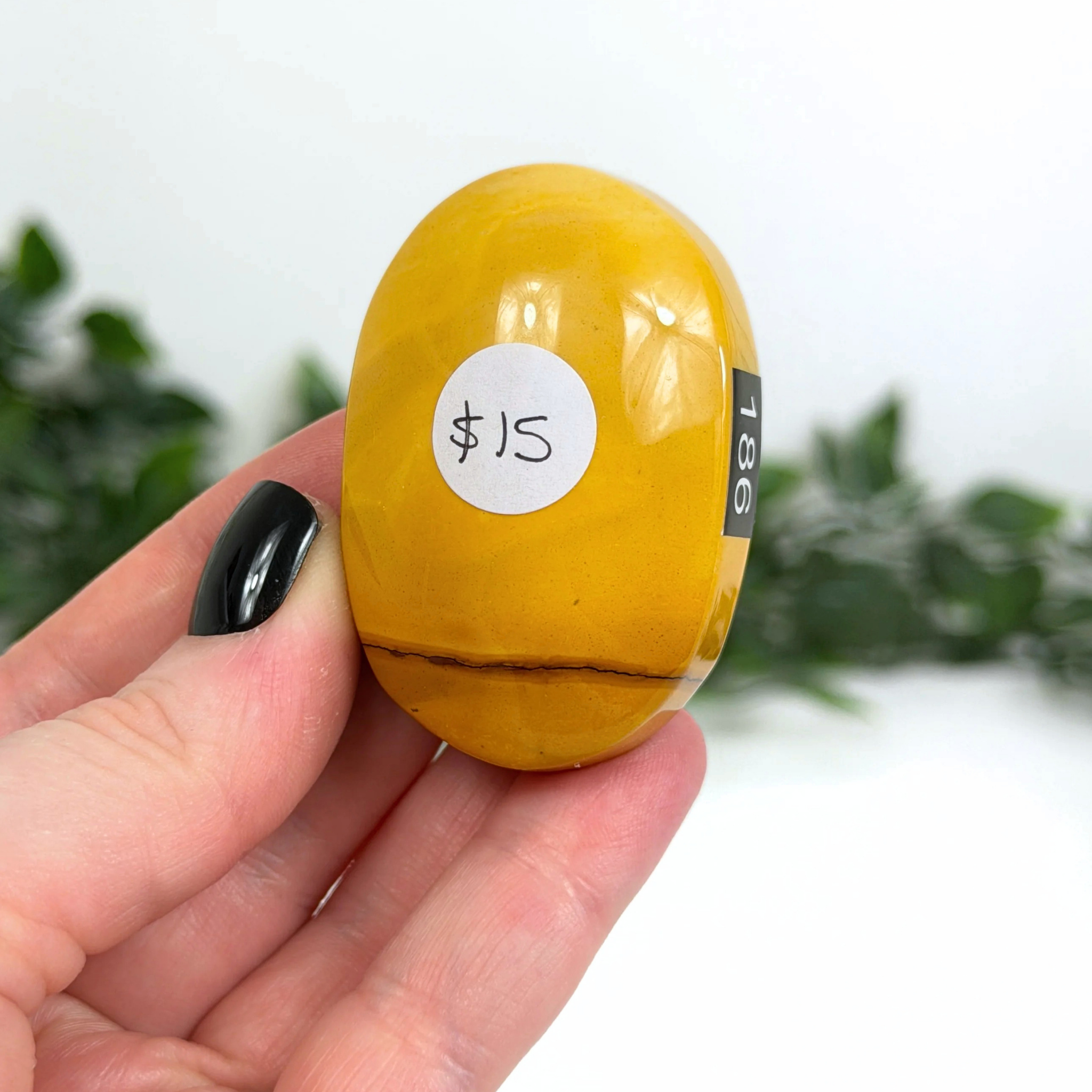 Yellow mookaite palm stone with a price tag held in a hand against a blurred green background