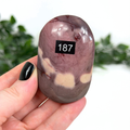Purple mookaite palm stone held in a hand with a blurred green background
