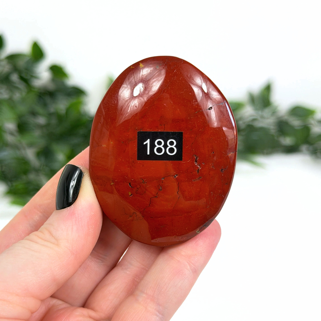 Red mookaite palm stone held in a hand with a blurred green background