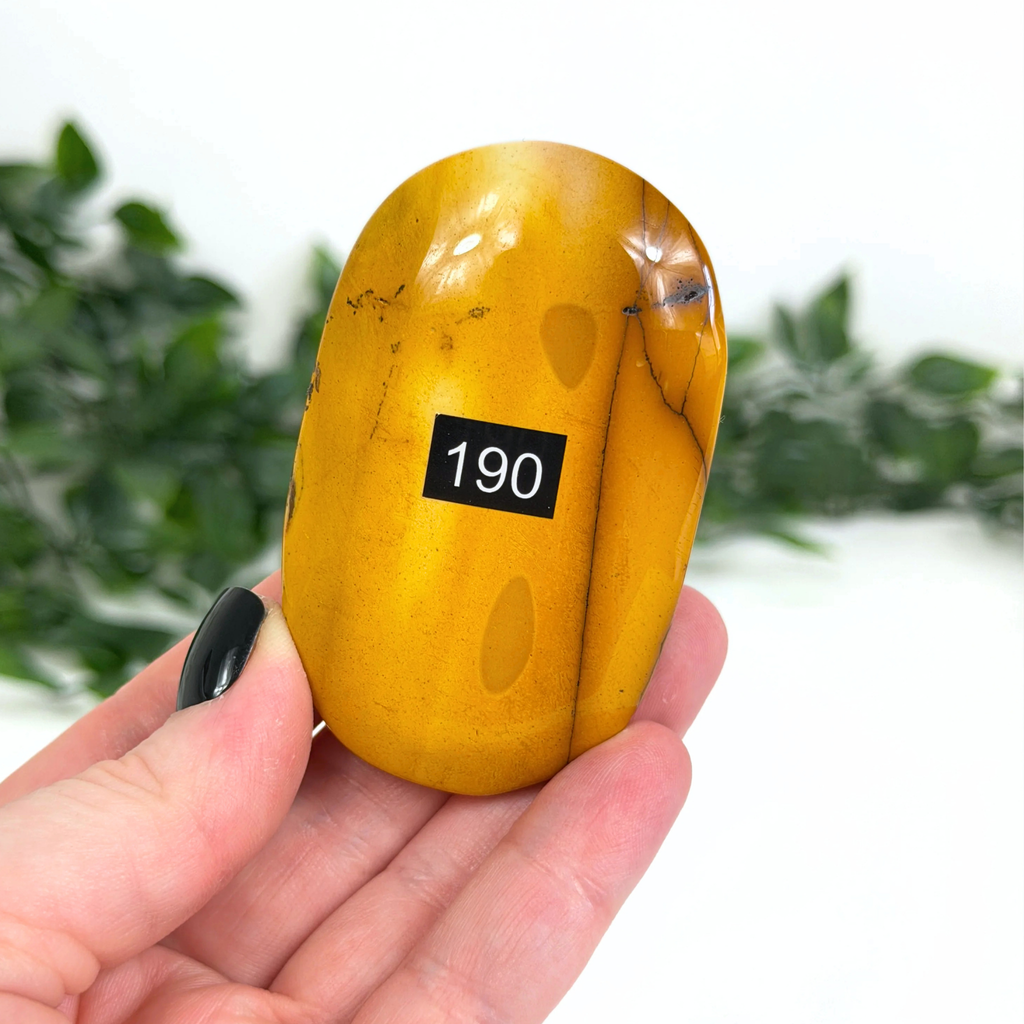 Yellow mookaite palm stone held in a hand against a blurred green background