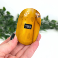 Yellow mookaite palm stone held in a hand against a blurred green background