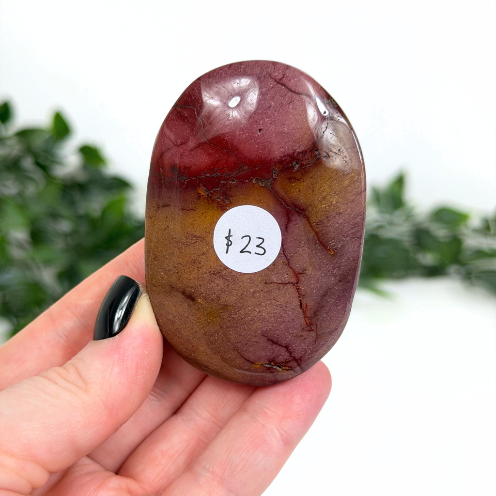 Mookaite palm stone held in a hand with a blurred green background