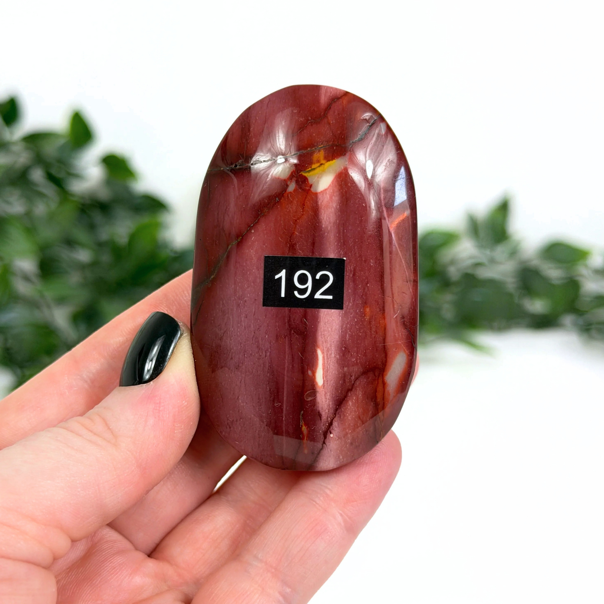 Red mookaite palm stone held in a hand with a blurred green background