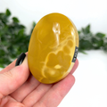 Hand holding a yellow mookaite palm stone with '193' on a white background