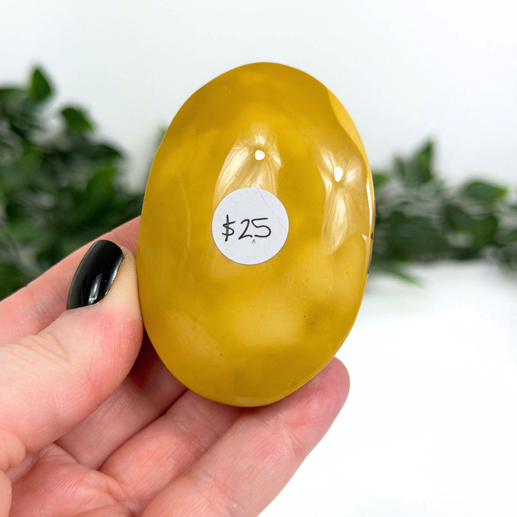 Yellow mookaite palm stone with a price tag held in a hand against a blurred green background