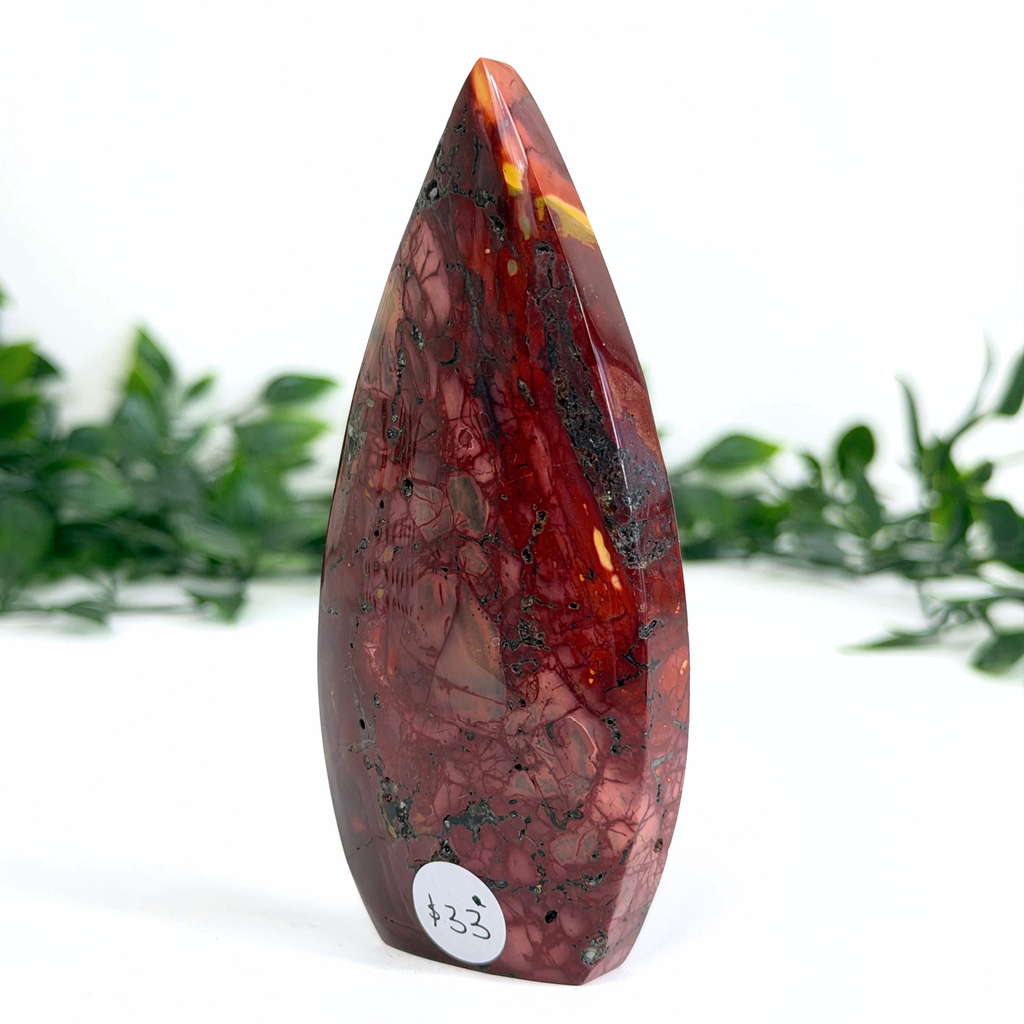 Marbled red and black mookaite teardrop stone with a white label on a white background