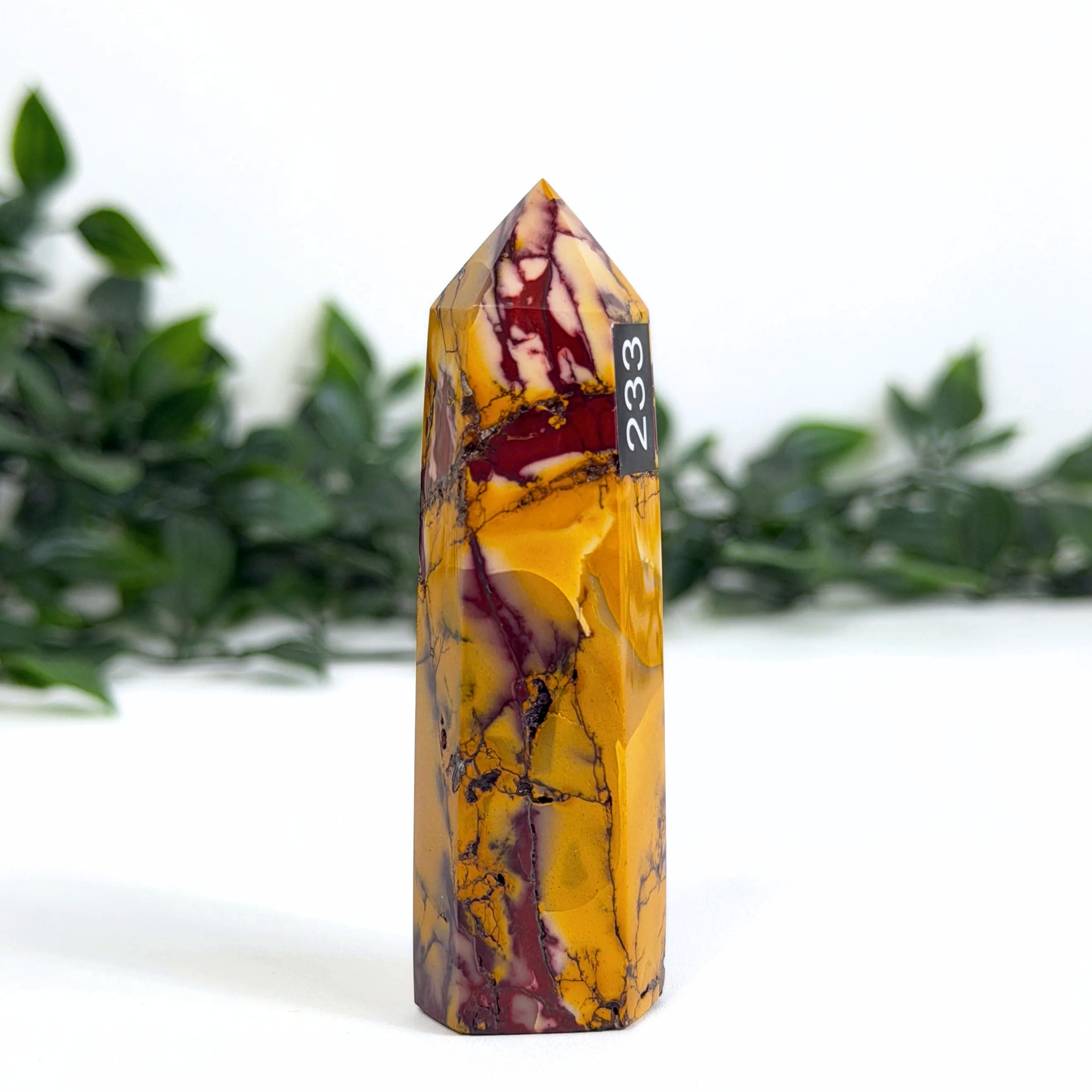 Marbled mookaite crystal tower with '233' on a white background with greenery
